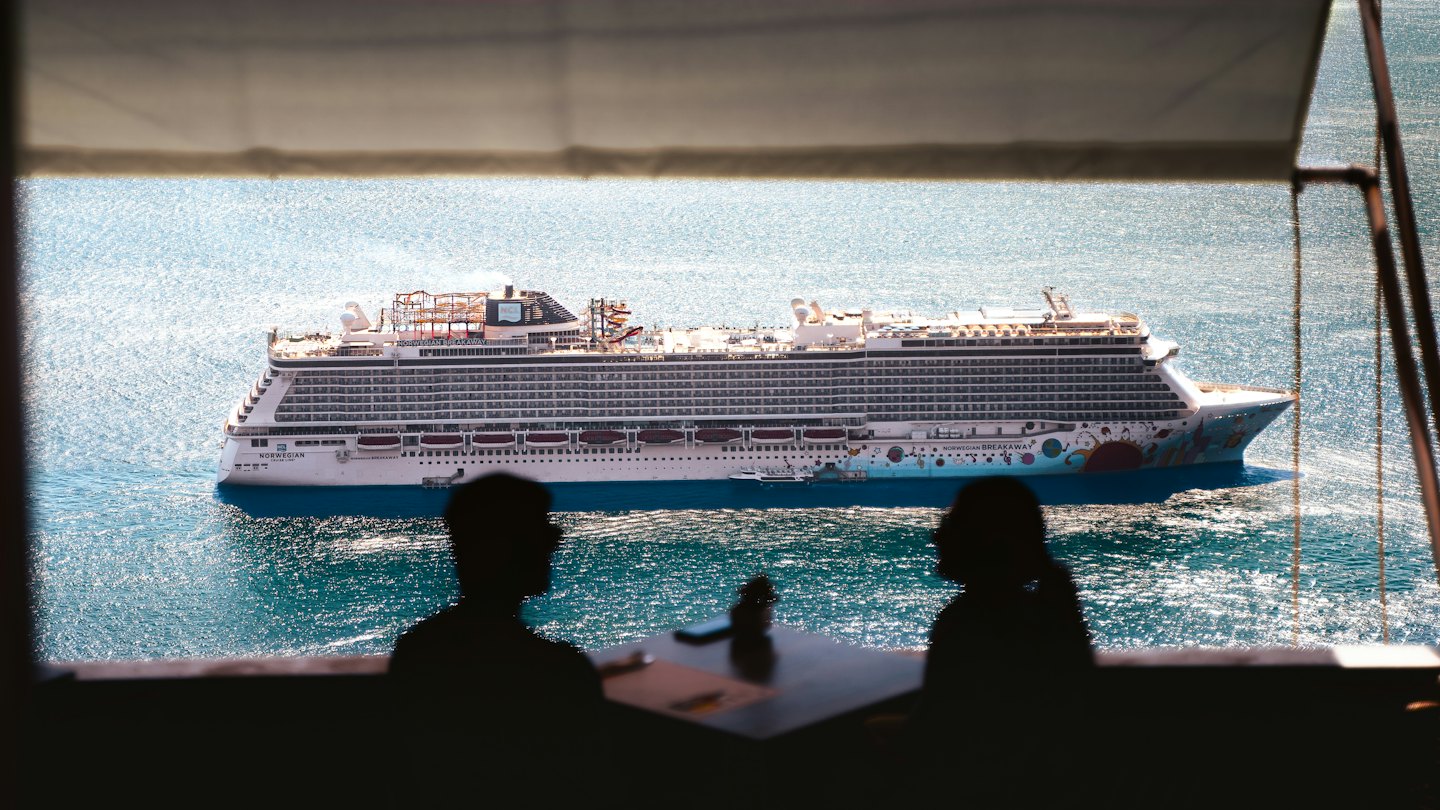Zwei Personen beobachten von einem Balkon aus ein großes Kreuzfahrtschiff.
