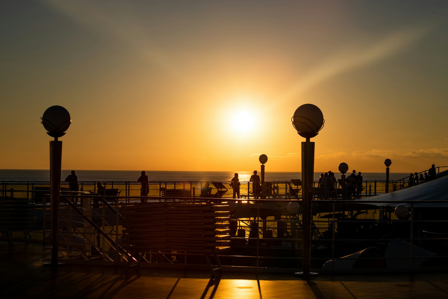 Passagiere auf dem Deck eines Kreuzfahrtschiffes sehen den Sonnenuntergang über dem Meer.